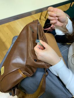 Student smiling to camera, sat at a sewing machine and holding up fabric